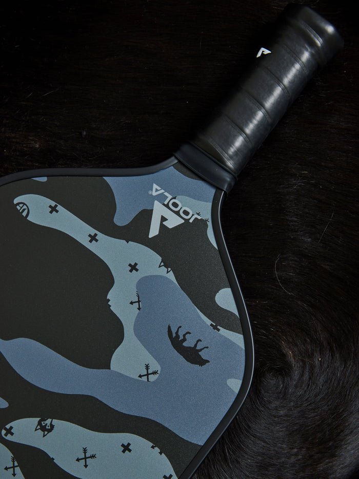 G.O.A.T. Camo Pickleball Paddle in Shepherd - Lifestyle Flat Lay on Dark Fur, Camo Surface Detail | Greyson Clothiers