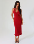 A person with long dark hair is wearing the TIGERMIST GRANGER MIDI DRESS in cherry red, featuring a sleeveless, halter-neck design with a ruffled hem. They are standing against a plain white background and are accessorized with black high-heeled sandals and a gold bracelet.