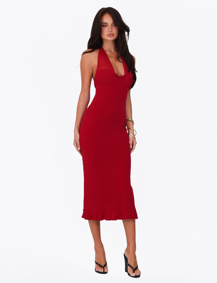 A woman with long dark hair is wearing the Cherry Red Granger Midi Dress by Tigermist, along with black high-heeled sandals. She poses against a plain white background with her hand on her hip, looking directly at the camera.