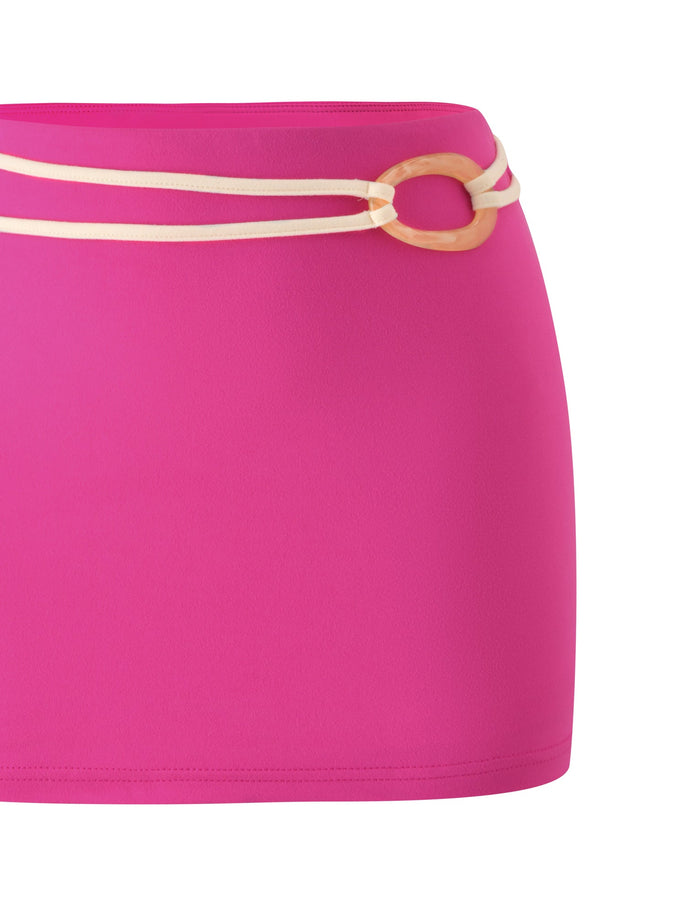 The GREER MINI SKIRT by TIGERMIST is a vibrant hot pink mini skirt accented with a beige double-string belt and a round wooden buckle, styled against a white background—ideal for transitioning effortlessly from beach to bar.
