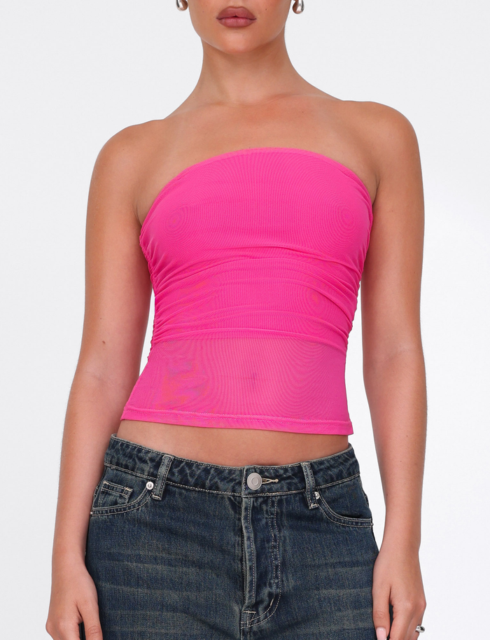 A person models the TIGERMIST HARRIETT TUBE TOP - PINK, a strapless, bodycon pink top, paired with high-waisted blue jeans and shown from shoulders to hips against a white background.