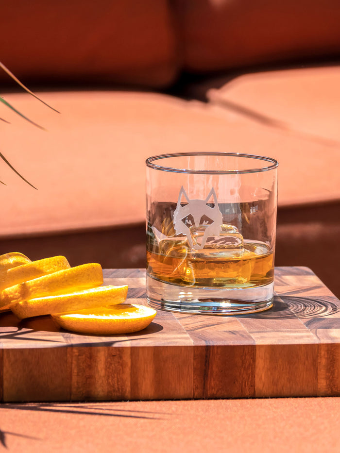 Icon On The Rocks Glass with whiskey and ice on wood board, wolf etching detail, orange slices - Lifestyle | Greyson Clothiers