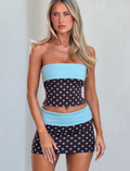 A woman poses against a light background wearing the TIGERMIST IMOGEN TUBE TOP in brown and blue polka dot, a strapless mini dress with solid light blue bands at the top and waist for a chic look.