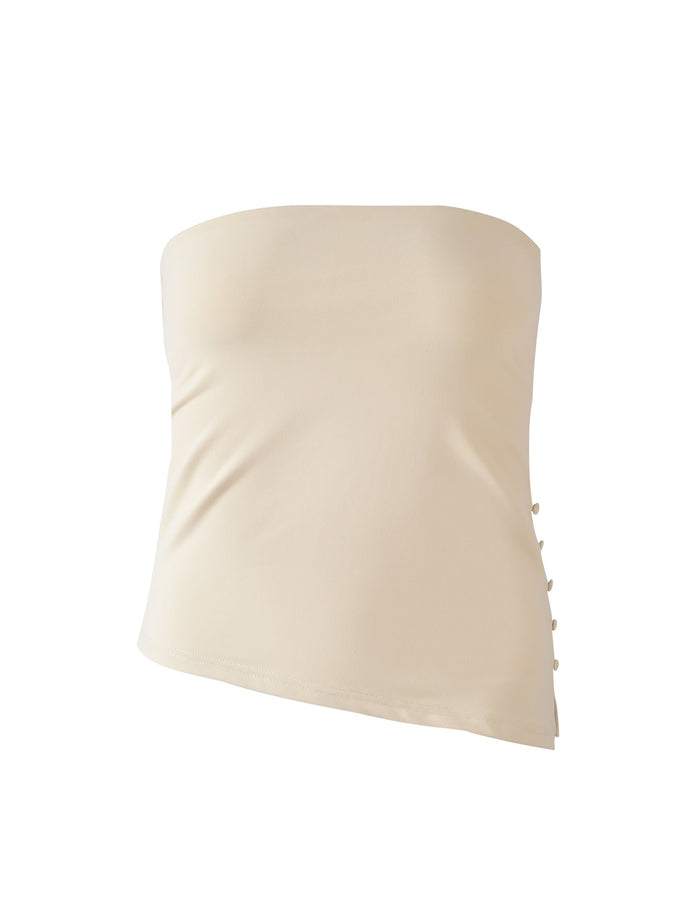 The INDIRA TOP - CREAM by TIGERMIST is a beige strapless top with a fitted silhouette, side decorative buttons, and an elegant asymmetrical hem.