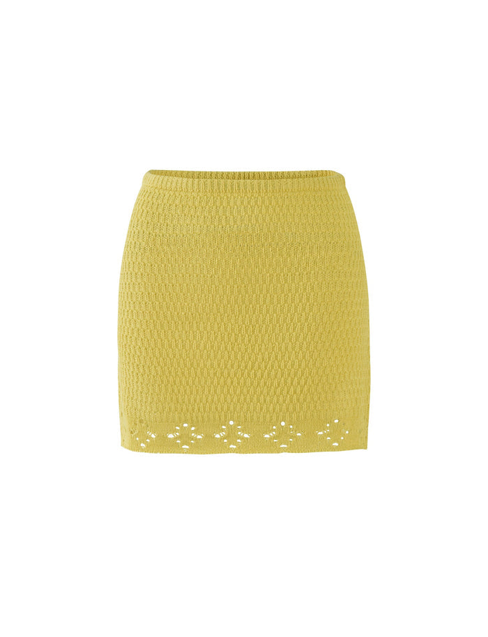 The JANAI SKIRT - YELLOW: LEMON from TIGERMIST is a yellow, textured knit skirt with a slightly tapered silhouette. It features a small, delicate floral cutout pattern along the hemline. The design is simple and elegant, with no visible buttons or zippers. The fabric has a subtle woven texture.