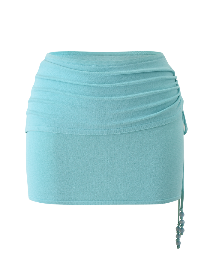 The TIGERMIST JASMINA KNIT MINI SKIRT - BLUE features a light blue knit fabric, ruched waistband, fitted silhouette, and beaded side drawstring ties, shown against a plain white background.