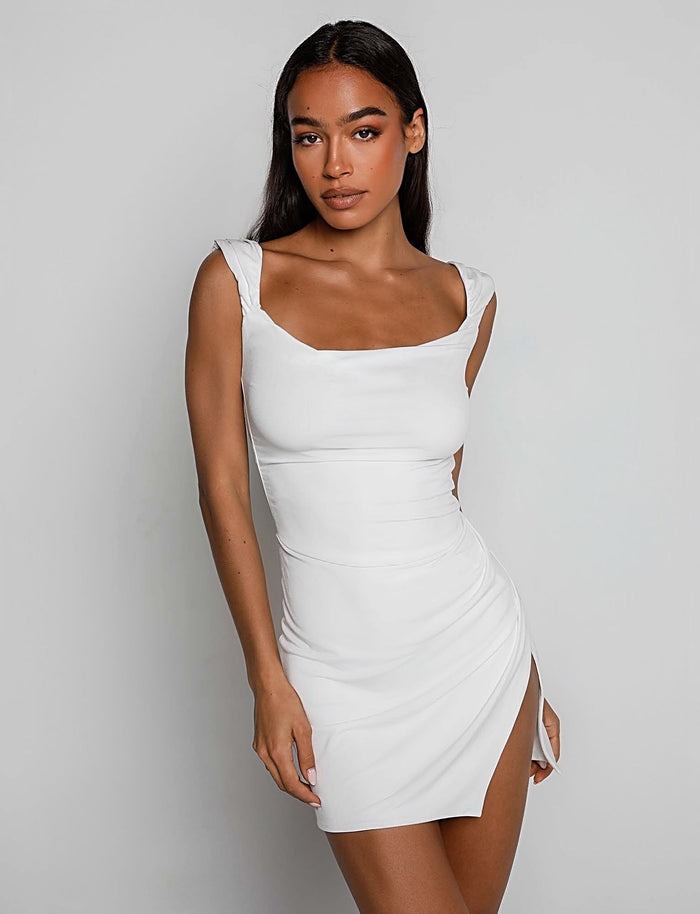 A woman is posing against a plain background, wearing the JOSLIN DRESS - WHITE from TIGERMIST. The dress is fitted, sleeveless with a square neckline and features a high slit on one side. She has long dark hair and a neutral expression.