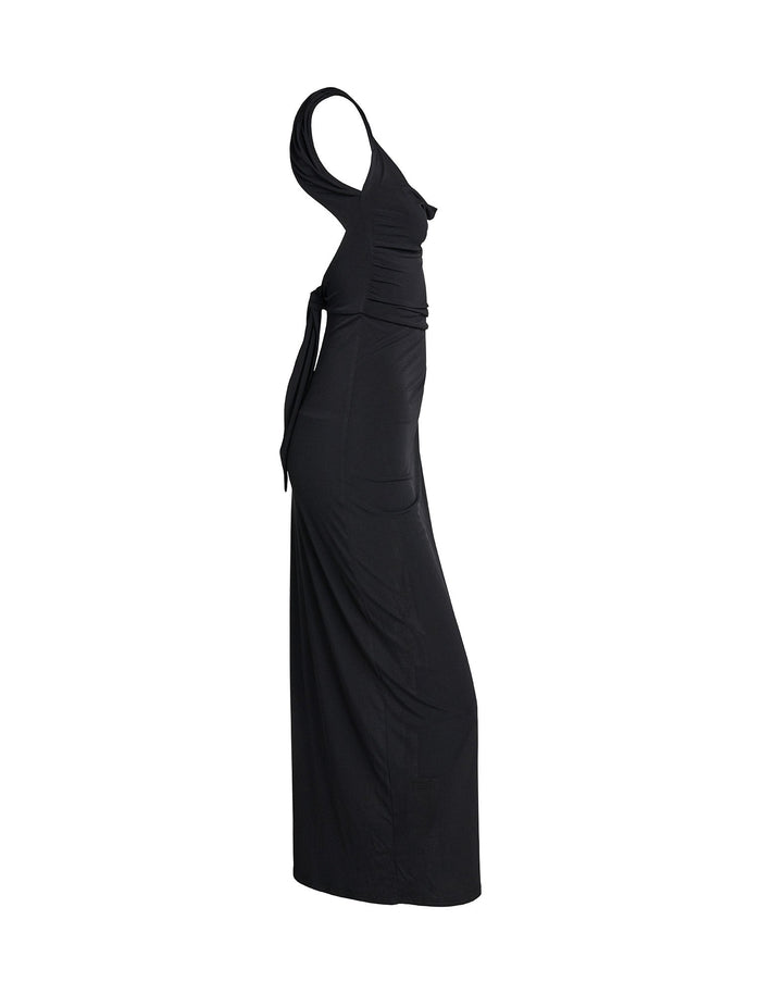 A side view of the JOSLIN MAXI DRESS - BLACK from TIGERMIST is shown on a white background. This long, form-fitting, black sleeveless dress features a cinched waist and a draped design on the torso, creating elegant, flowing lines.