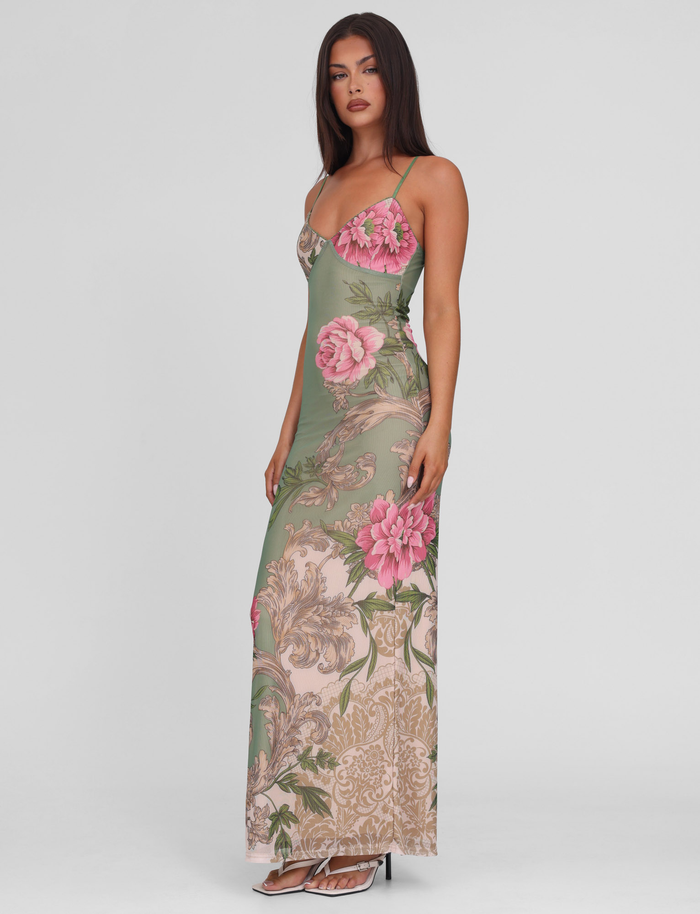 A woman models the TIGERMIST JULIANNA DRESS in Green Rococo Floral—a long, fitted maxi dress with adjustable spaghetti straps, featuring a green base with large pink florals and ornate beige patterns—against a white background.