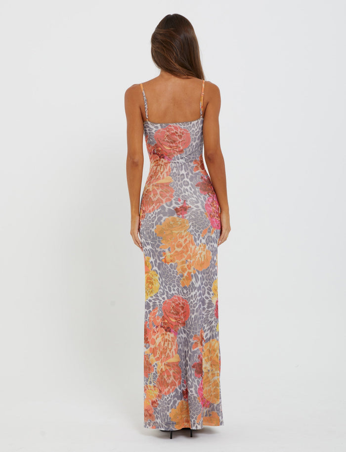 A person with long, brown hair is wearing the sleeveless ankle-length JULIANNA DRESS from TIGERMIST, featuring a vibrant multi-color print with leopard and orange leopard patterns. They are standing with their back to the camera against a plain white background.