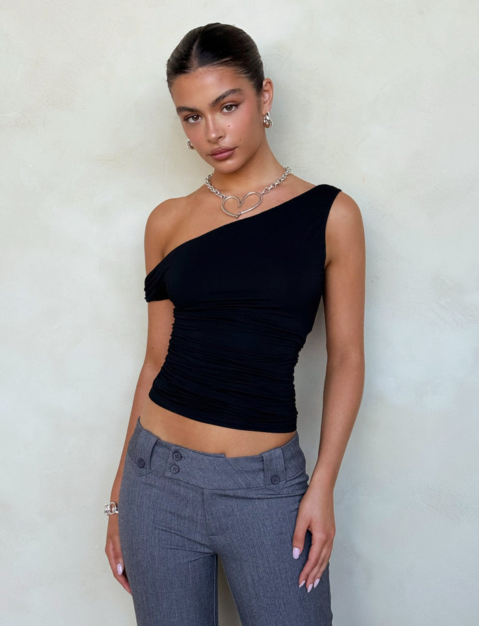 A person with long hair tied back is standing against a plain background wearing a TigerMist KADENCE TOP in black and gray high-waisted pants. They have a necklace with interlocking rings and are posing with one hand resting at their side.
