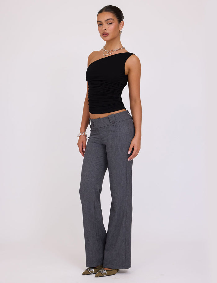 A person stands facing forward, wearing the KADENCE TOP - BLACK and gray flared pants from TIGERMIST. They have their hair pulled back and are accessorized with a necklace, bracelet, and earrings. They are standing on a plain white background.