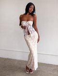 A woman poses indoors against a light wall wearing the Tiger Mist USA CL - KAROLINA TOP, a sheer white lace strapless top paired with a matching long skirt, styled with white high-heeled sandals and large hoop earrings.