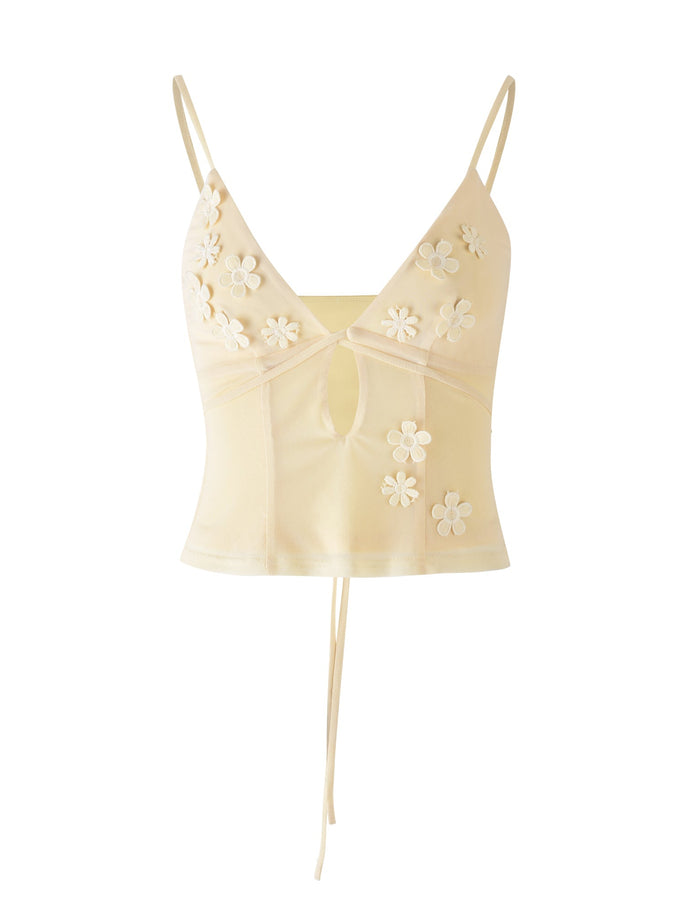 The "KATINA CAMI - YELLOW : BUTTER" from TIGERMIST is a light beige camisole with thin shoulder straps, featuring a V-neckline, floral applique detailing, and a small keyhole cutout in the center. The top also has an adjustable tie at the back.