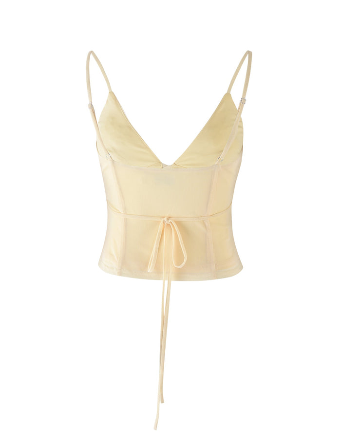 The Katina Cami - Yellow : Butter from Tiger Mist is a light yellow, sleeveless, V-neck cropped top featuring thin adjustable straps and a front tie detail at the waist. The fabric appears to be slightly sheer and lightweight.