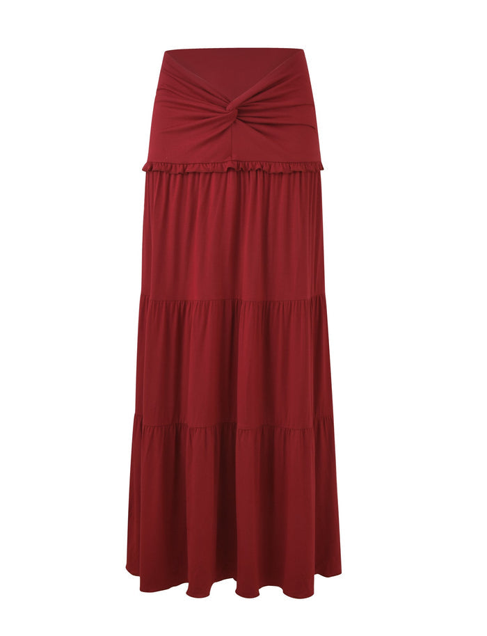 The KATYA MAXI SKIRT by TIGERMIST in red features a wide waistband, tiered panels with a knotted detail at the waist, and flowing layers. Its lightweight fabric offers a casual vibe suitable for various occasions.