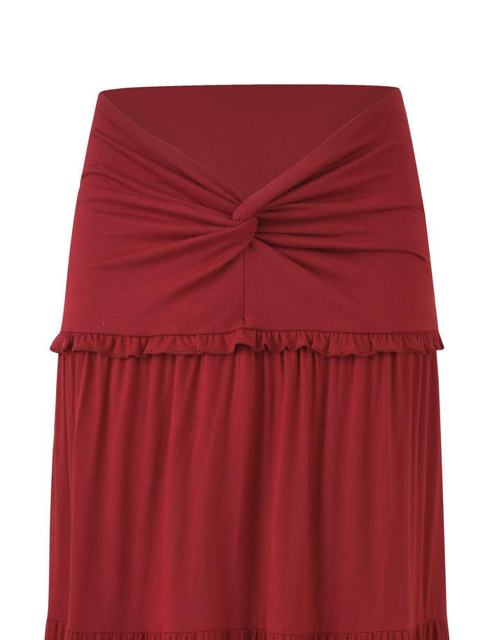 The KATYA MAXI SKIRT - RED by TIGERMIST showcases a twisted knot design at the wide waistband, tiered panels for subtle ruffles, and elegant draping soft fabric.