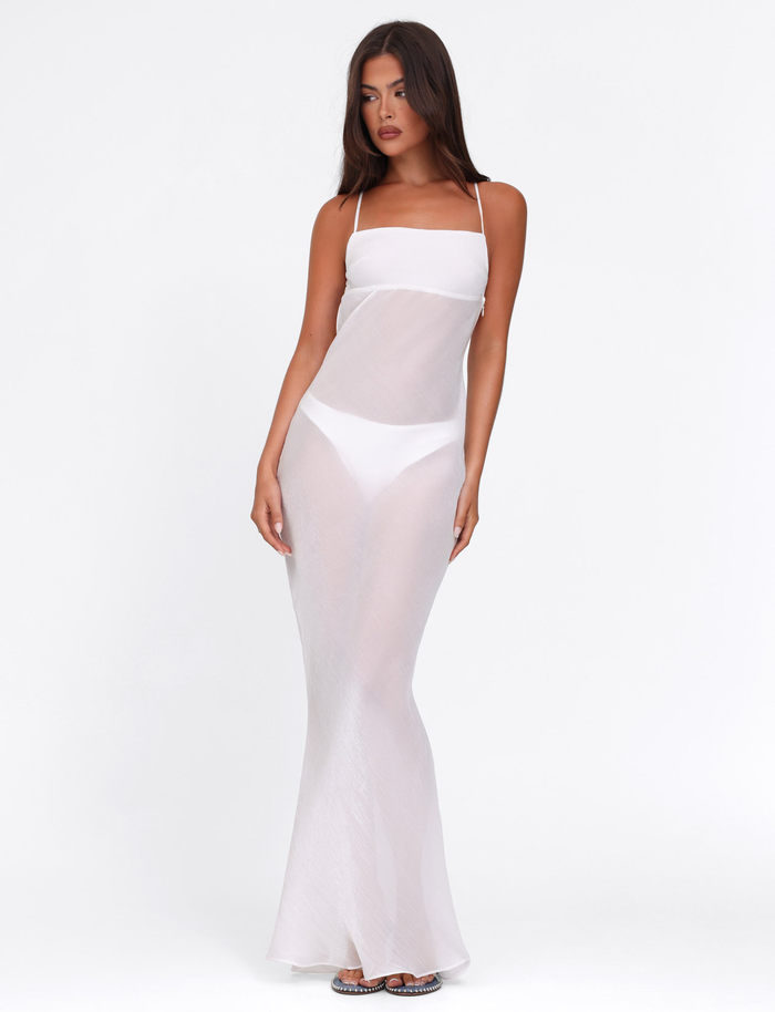 A woman poses against a white background wearing the TIGERMIST KIAH MAXI DRESS - WHITE : ICE over a white bikini. She has long brown hair, minimal accessories, and gazes slightly to the side.