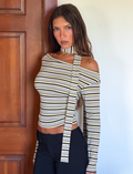 A woman with long brown hair wears the TIGERMIST KIERSTEN SCARF TOP - MULTISTRIPE, featuring a matching choker, as she stands in front of a wooden door and white wall, looking at the camera with a serious expression.