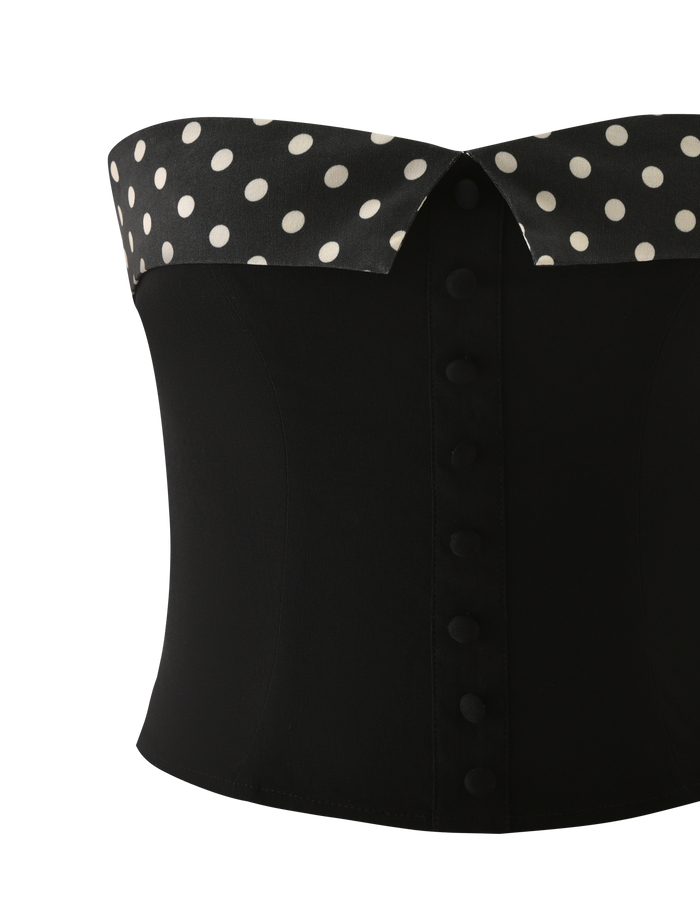 The TIGERMIST KITTIE 2.0 BUSTIER - BLACK is a strapless corset with a black and white polka dot folded-over neckline, crafted from stretch suiting fabric and detailed with covered buttons down the front.