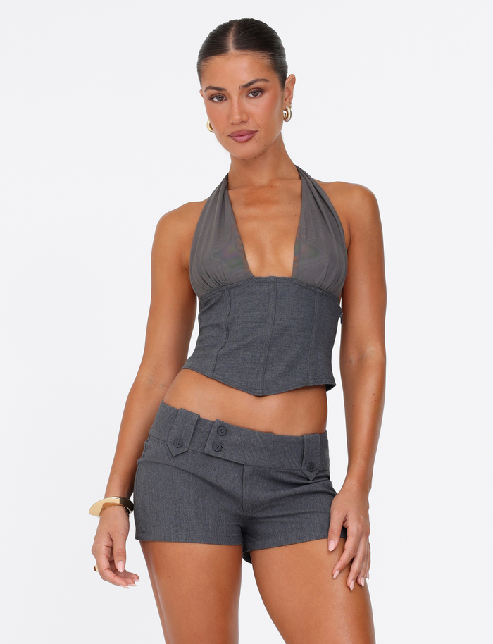A woman poses confidently in the TIGERMIST KITTIE SHORT - GREY, a high-waisted, button-detailed suiting short paired with a matching sleeveless deep V-neck halter top, styled with gold hoop earrings and a bracelet, against a white background.