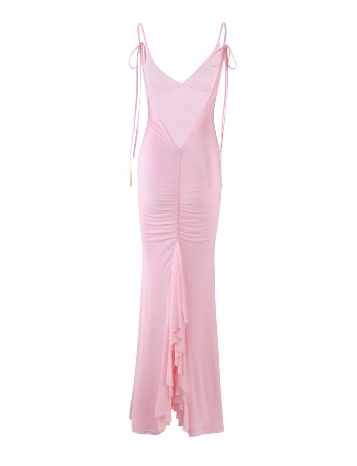 The KYLAH DRESS in BABY PINK by TIGERMIST is a floor-length masterpiece featuring a deep V-neck back, spaghetti straps tied at the shoulders, and gathered fabric that creates a ruched effect down the center. The dress showcases a cascading ruffle at the back, adding texture and movement.