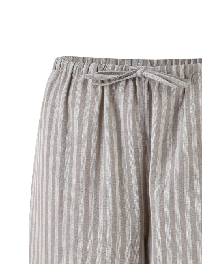 Image shows a close-up view of the LAINEY PANT - GREY : STRIPE from TIGERMIST. These light grey and white vertically striped drawstring pants feature a bow-tied drawstring at the waistband, and the fabric appears soft and comfortable.