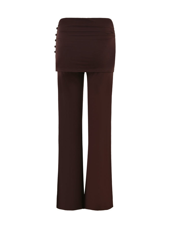 The LEILANI PANT - BROWN : CHOCOLATE by TIGERMIST is a stylish pair of chocolate high-waisted wide-leg pants featuring a fitted mini skirt overlay. The flared leg design includes button detailing on the left side. Made from high stretch fabric, these pants offer a smooth and elegant appearance, sitting flat against the surface.