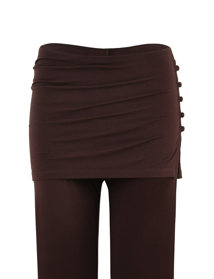 The LEILANI PANT - BROWN : CHOCOLATE by TIGERMIST showcases a ruched mini skirt overlay alongside decorative buttons on one side, with a flared leg design crafted from high stretch fabric. These pants are photographed against a plain white background.
