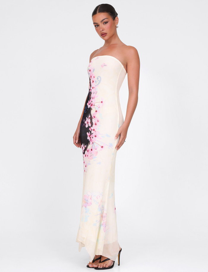 A woman models the TIGERMIST LILLIAN MAXI DRESS – MULTI : FLORAL : CHERRY BLOSSUM, a strapless high-stretch mesh dress with pink cherry blossom floral patterns and black accents, paired with heels against a plain white background.