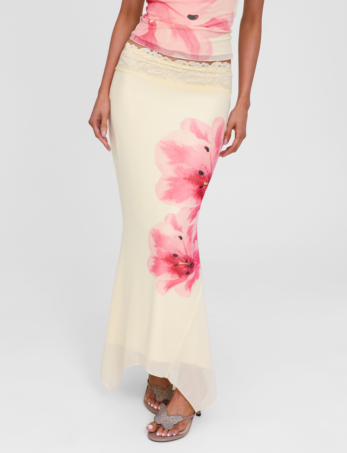 A person wearing the TIGERMIST LILLIAN SKIRT in yellow, featuring a pink floral print and lace trim waistband, paired with a matching floral top and butterfly sandals.