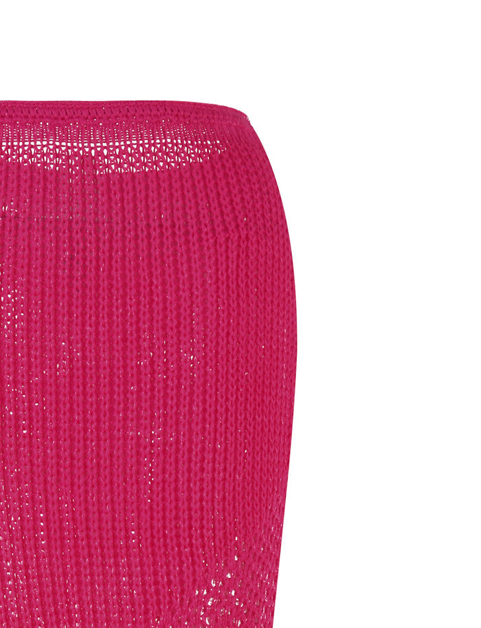 A knitted or crocheted fabric in hot pink is shown, appearing to be a tubular piece of clothing, likely the MACAULEY SKIRT. The slightly open weave allows light to pass through, highlighting its bodycon silhouette. This product is by TIGERMIST.