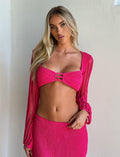 A woman with long blonde hair is wearing the vibrant hot pink MACAULEY TOP from TIGERMIST and a matching skirt, both featuring a bodycon silhouette. She stands against a plain light-colored wall.