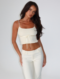 A woman with long dark hair poses against a plain white background, wearing the TIGERMIST MAISIE TOP in pale yellow, featuring adjustable shoulder straps.