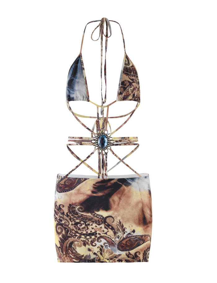 A trendy Tigermist two-piece set from the MARCEL DRESS collection, featuring a halter neck bikini top with intricate straps and a gemstone detail at the center. The set includes a matching high-waisted skirt adorned with an abstract, paisley tie-dye print in earthy tones of brown, beige, and black.