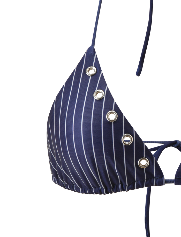A close-up of the TIGERMIST MARREN BIKINI TOP - NAVY PINSTRIPE features white vertical stripes and silver grommet details on one triangle cup, set against a plain white background. This adjustable halter top ensures a stylish, customizable fit.