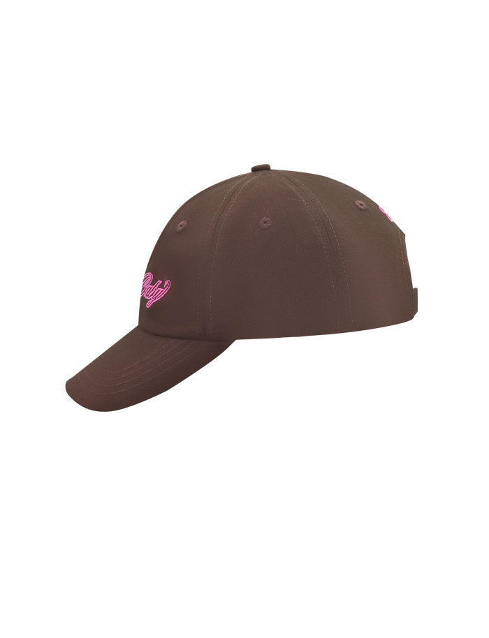 The MERRYN CAP - CHOCOLATE by TIGERMIST is a brown 5 panel hat with pink embroidered lettering on the front, displayed from a side angle against a plain white background.