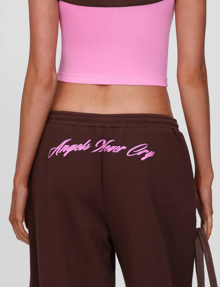 A person wears TIGERMIST's MERRYN TRACK PANT in chocolate with "Angels Never Cry" in pink cursive on the back, highlighting the wide leg style.