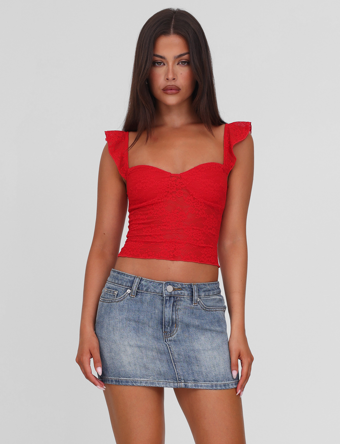 A woman with long brown hair wears a red lace crop top and the TIGERMIST MICHAYLA MINI SKIRT in mid wash, styled with five pockets, standing against a plain white background.