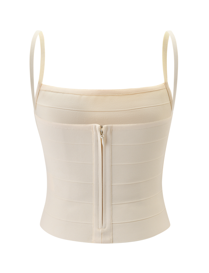 The MIDORI BANDAGE TOP in cream by TIGERMIST features thin shoulder straps, horizontal seam details, and a central front zipper. The structured fabric provides a fitted, streamlined silhouette for a flattering look.