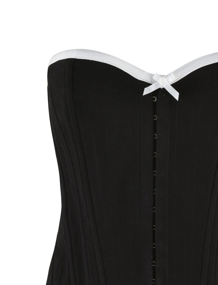 Close-up view of the TIGERMIST MILLIE CORSET 2.0 - BLACK, a strapless black denim corset with white ribbon trim along the top edge. The bodycon fit features vertical boning for structure and a row of hook-and-eye closures down the center front, with a small white decorative bow placed in the middle at the top.