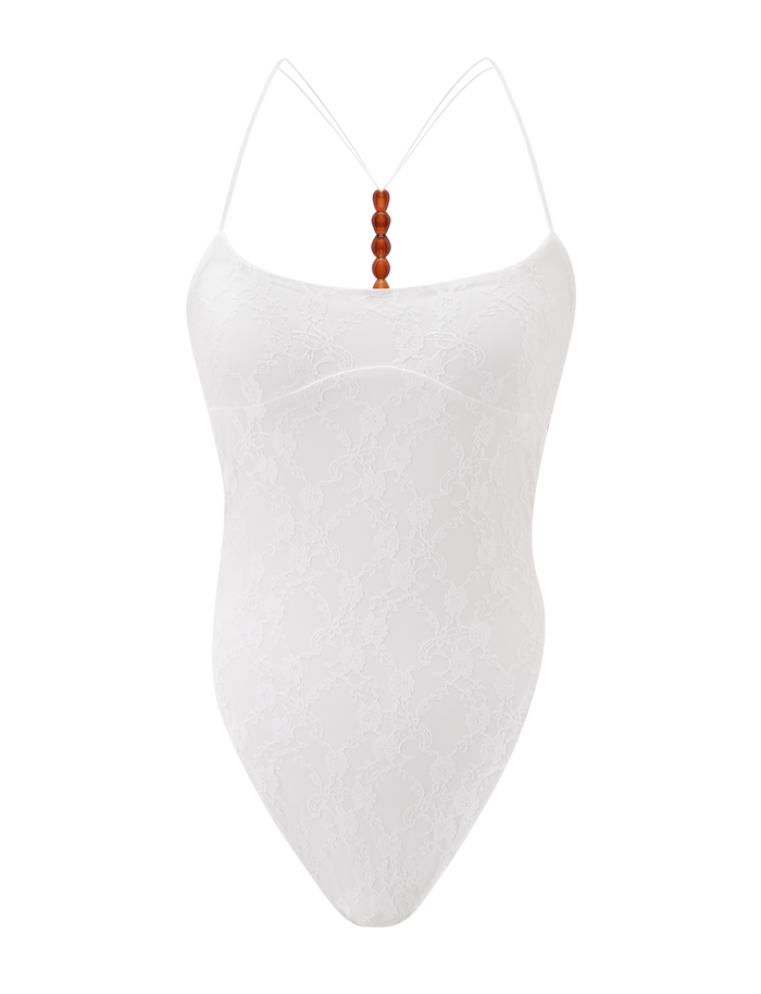 The MINERVA 2.0 BODYSUIT by TIGERMIST features cream lace, thin spaghetti straps, a G-string bottom, and brown beads at the center neckline, shown on a plain white background.