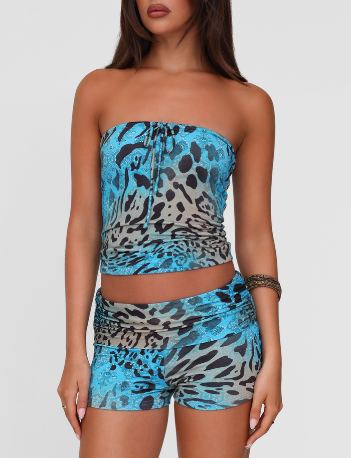 A woman with long brown hair wears the TIGERMIST MIRELY TOP - MULTI : LEOPARD : LEOPARD SWIRL and matching high-waisted shorts, accessorized with a bangle, standing against a plain white background.