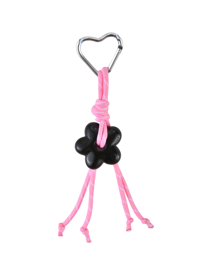 The MIRIAM KEYCHAIN - HOT PINK by TIGERMIST features a heart-shaped clasp carabiner, pink cords knotted around a black flower-shaped charm, and four loose cord ends, all set against a white background.