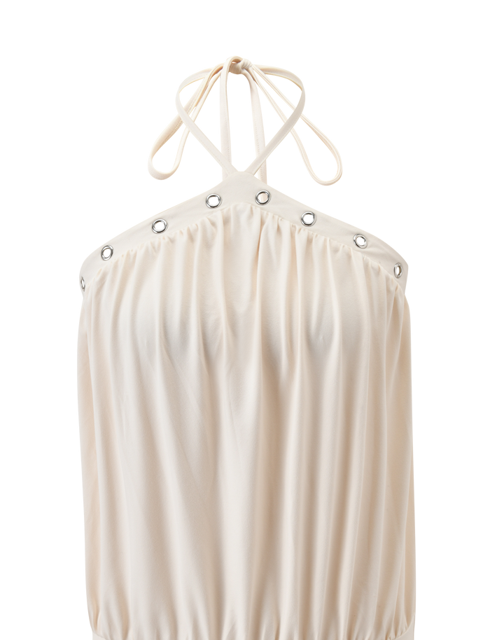 The NATASHA DRESS by TIGERMIST in cream features a halter neckline with thin cross-neck straps, silver grommet details, gathered loose fit, and soft flowing fabric.