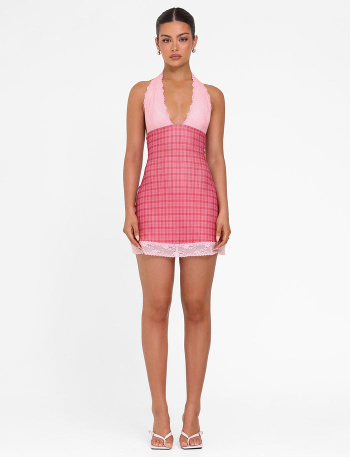 Against a white backdrop, a person showcases the TIGERMIST NAVIA DRESS in red check—a halter mini dress with lace trim and a plunging neckline. Their hair is neatly styled back, and they are sporting white sandals.