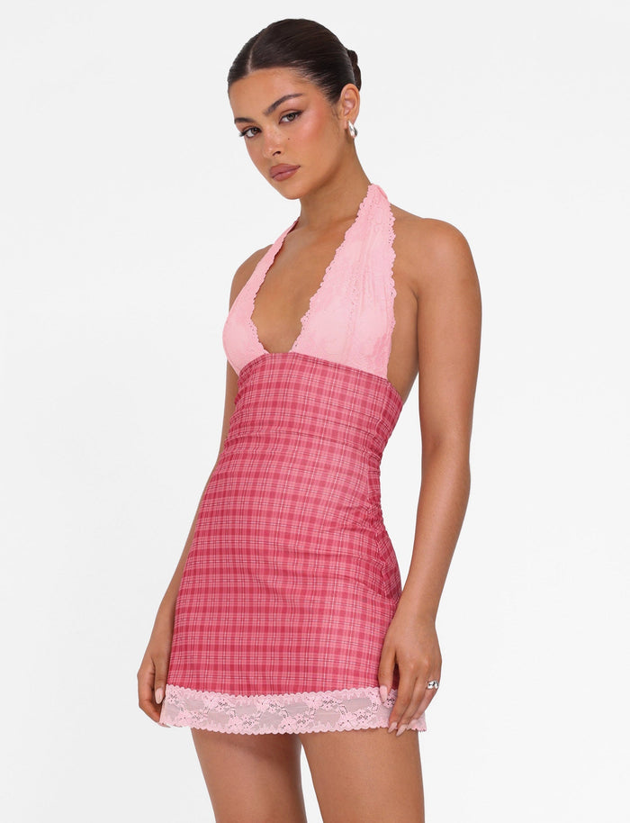 A person poses elegantly in the NAVIA DRESS - RED CHECK from TIGERMIST, featuring a delicate pink lace trim. Their hair is styled up, and they wear elegant earrings against a plain white background.