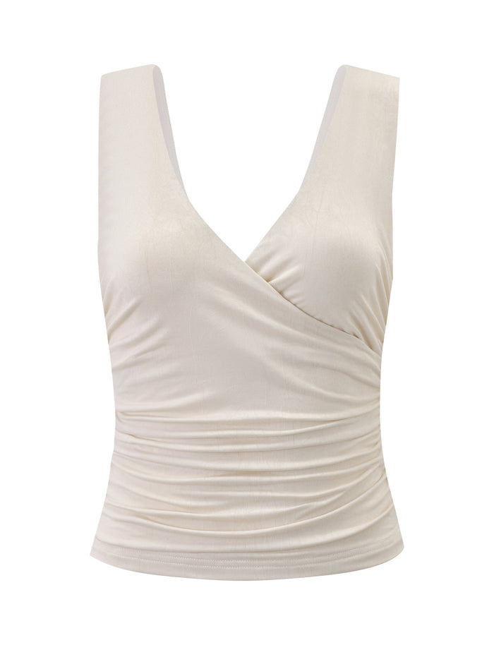 The NURA TOP - IVORY by TIGERMIST features a deep V-neck, crossover neckline, and wrap-style front with slight side ruching to flatter the waist. Its sleeveless design adds an elegant touch.