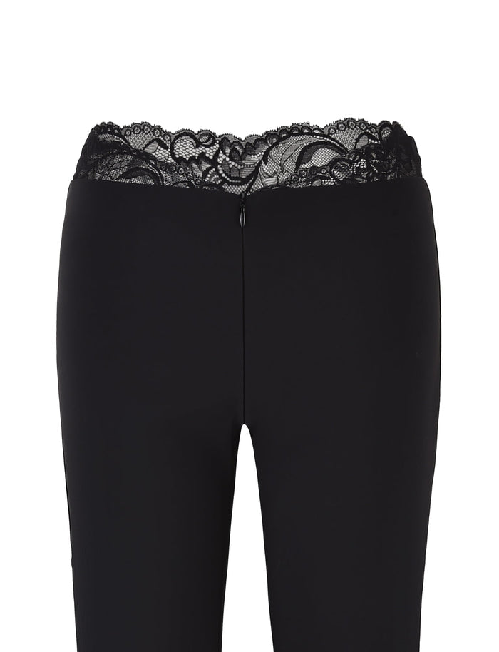 The NYOMI PANT - BLACK by TIGERMIST features a flared design with a lace detail waistband at the top, shown from the front.