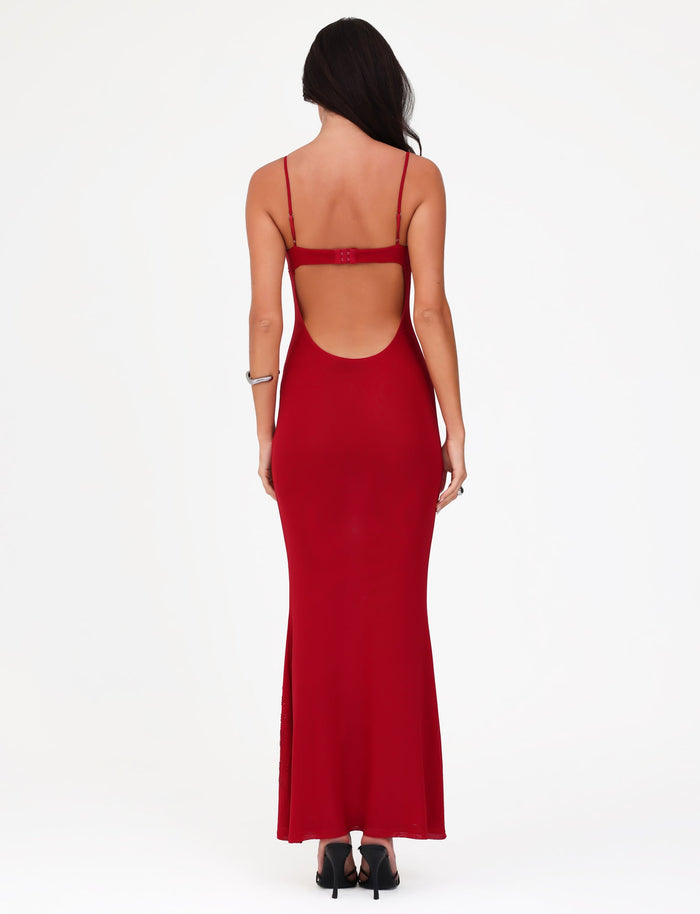 Rear view of a woman in a Tigermist Octavia Maxi Dress in Cherry Red, featuring a backless design with spaghetti straps, standing against a plain white background. The maxi-length dress pairs perfectly with her black heels and the bracelet on her right wrist. Her long hair cascades down her back, accentuating the elegant look.